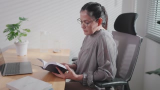 Woman sitting at desk with open window drinking coffee and reading a book enjoying the morning rainbow.	