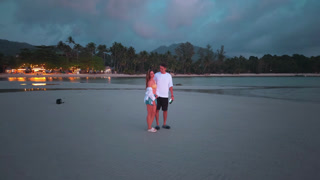 Happy couple walking hand in hand on tropical beach at sunset. Man and woman enjoying romantic vacation travel near ocean with palm trees