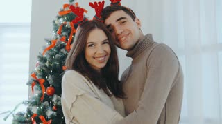Happy couple celebrating Christmas with festive antlers in front of a decorated tree at home during the holiday season