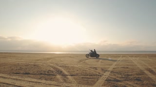Guy with a girl on a motorcycle in the desert. Couple riding on vintage motorcycle and having a good time at sunset on a dry salt lake. Slow motion shot
