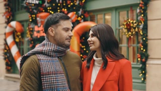 Caucasian couple smiling in a winter decorated street. They're enjoying time together, looking at the camera. Valentine's Day and festive