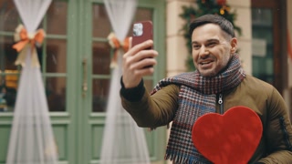 caucasian bearded man is video calling his parents showing the red shapes gift for his wife on the valentines day. happy male using