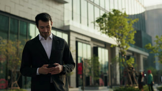 Portrait of focused Hispanic man office employee reads message on smartphone standing on sunset street. Young Latin businessman texts on