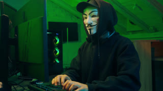 Lviv, Ukraine - June 03, 2024: Hacker anonymous typing computer looking at camera pointing finger programmer attack cyberspace fraud burglar