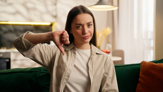 Upset frown frustrated dissatisfied Caucasian female lady girl woman indoors in living room at home at couch showing thumb down gesture
