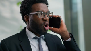 Angry mad African American business man yelling arguing talking mobile phone holding papers in office work documents mistake ethnic