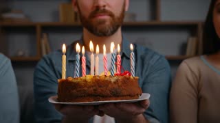 Close up unknown happy birthday man holding cake burning candles wishing smiling positive two multiethnic friends blowing in party blowers