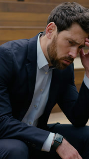 Vertical close up shot of Sad Caucasian businessman in suit thinking about problem with stressed expression while sitting in urban area