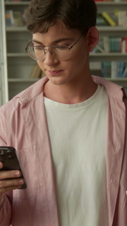 Caucasian teen man guy student choosing between book and mobile phone in library male teenage boy schoolboy confused puzzled pupil choose