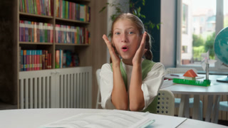 Happy wonder surprised Caucasian little girl child reading book studying learning looking at camera open mouth in school astonished pupil