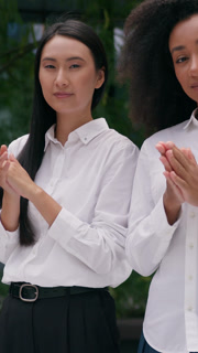 Diverse African Asian Korean business women clapping hands applauding outdoors in city celebrating congratulating two females colleagues