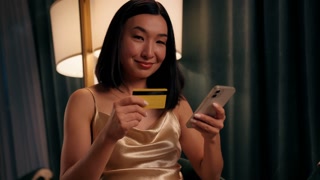 Happy smiling Asian woman shopping online with credit card payment with mobile phone Korean female Japanese Chinese lady indoors buying
