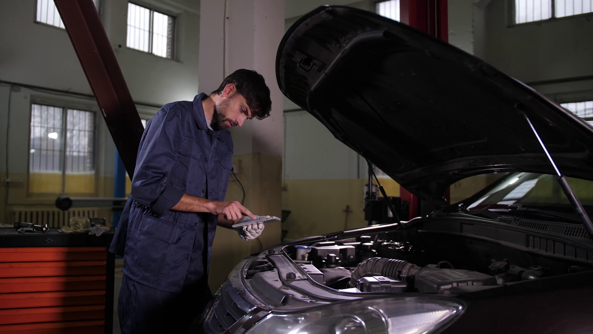 Auto repair service employee standing near opened car hood with tablet