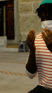 An African teenager with a mask on his face prays to Allah with his hands open at