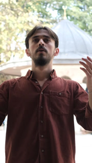 Young bearded Muslim praying with an open hand in the mosque courtyard, people who believe in Islam
