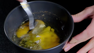 A person whisks egg yolks and powder in a black mixing bowl on a kitchen counter at Cooking, creating a frothy yellow mixture.