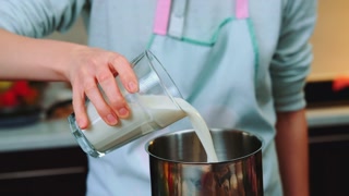 Woman pouring milk into an iron ladle. Close-up shot of table. Cooking in the kitchen