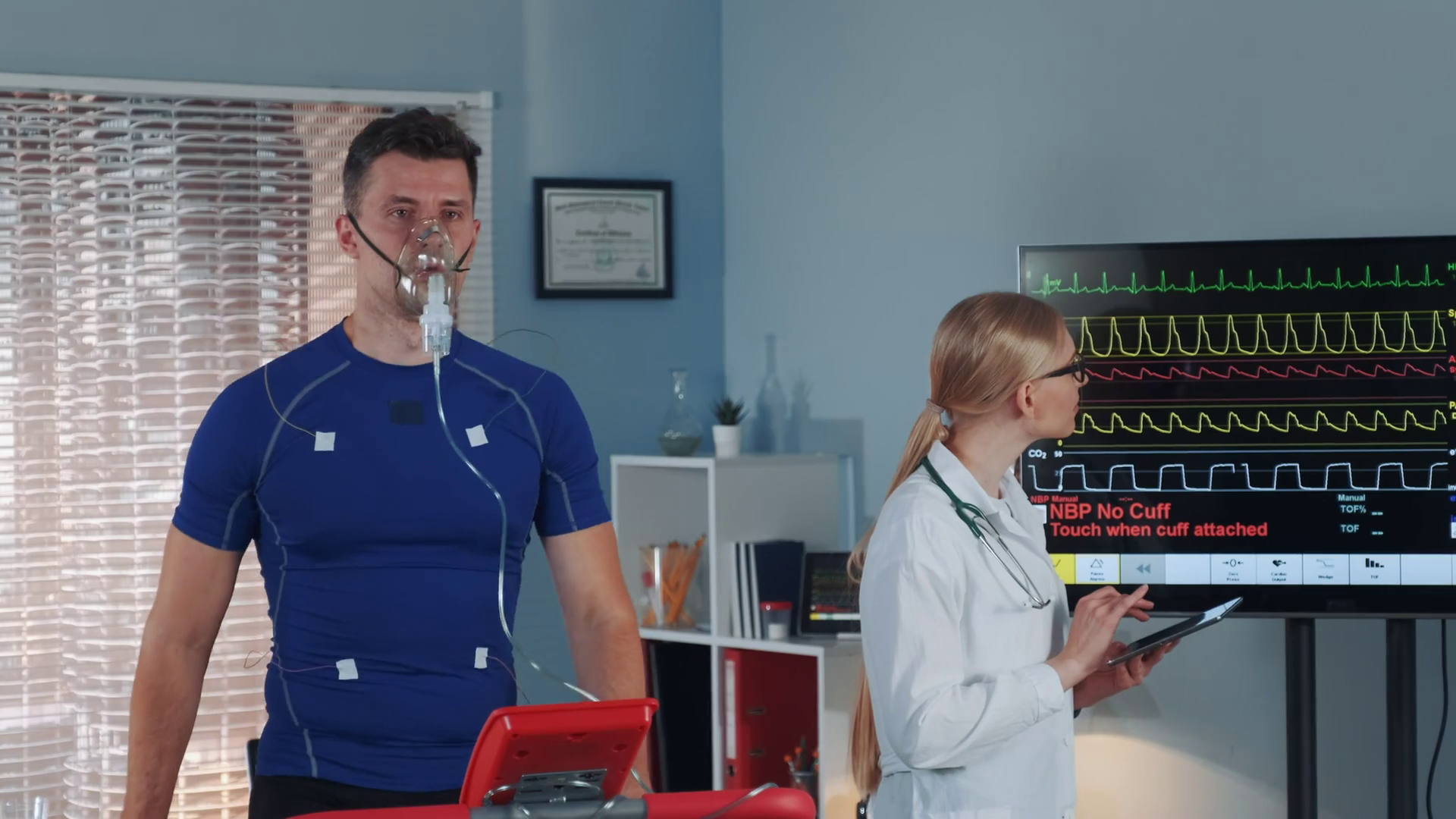 Athlete in oxygen mask doing stress test while cardiologist with tablet