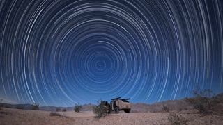 A teardrop camper trailer sits in the Anza Borego Desert as star trails fill the dark sky over the Thimble Trail area in California
