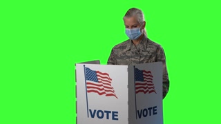 Conceptual green screen portrait of smiling woman military service Army member with face mask in voting booth at ballot box, careful decision for president in US election.