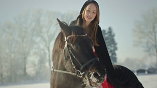 Beautiful woman in red dress riding black horse in winter