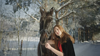 Beautiful woman hugging black horse in a winter forest
