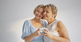 Cheerful positive wondered glad amazed mother and daughter enjoying holiday having big gift case in red package with white bow wearing casual outfits jeans isolated on grey background