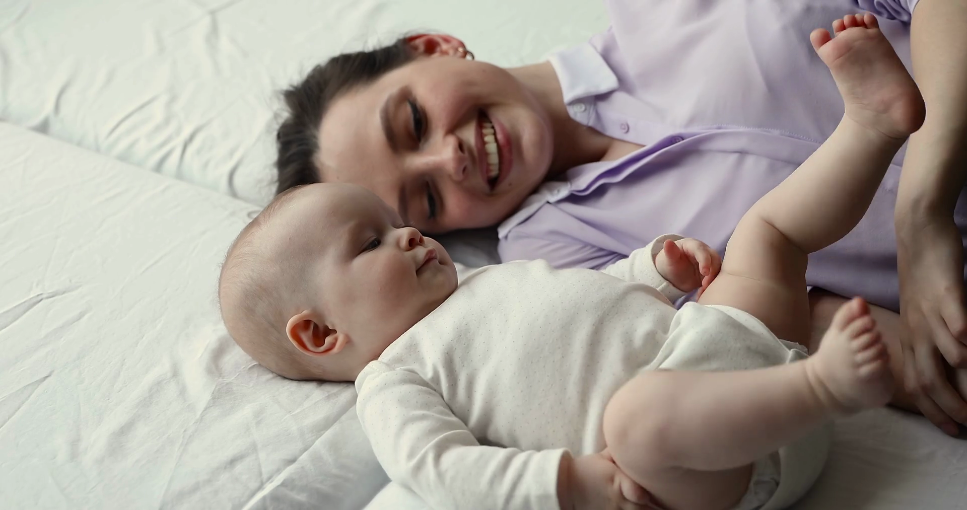 Mommy lying on bed watching baby kicking legs in air Stock Video