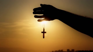 Male Hand is Holding Christianity Religion Symbol Cross in Sunset Light 