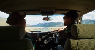 Young couple kissing in the front seats of their car while enjoying a road trip at sunset, driving through a beautiful desert landscape