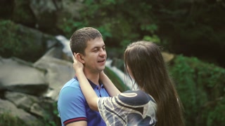 Loving Couple Walking Outdoors Near a Waterfall. Morning light shines into the camera. Slow morion