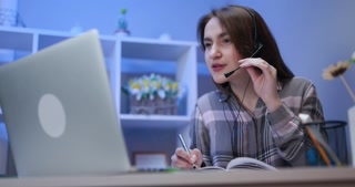 Happy girl in headphones speaking by webcam at webinar training look at laptop make notes. Girl student talking by video conference call, online teacher teaching consulting client e-coaching concept