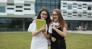 Two young female students walking and sharing books. Portrait shot. Happy students in school.