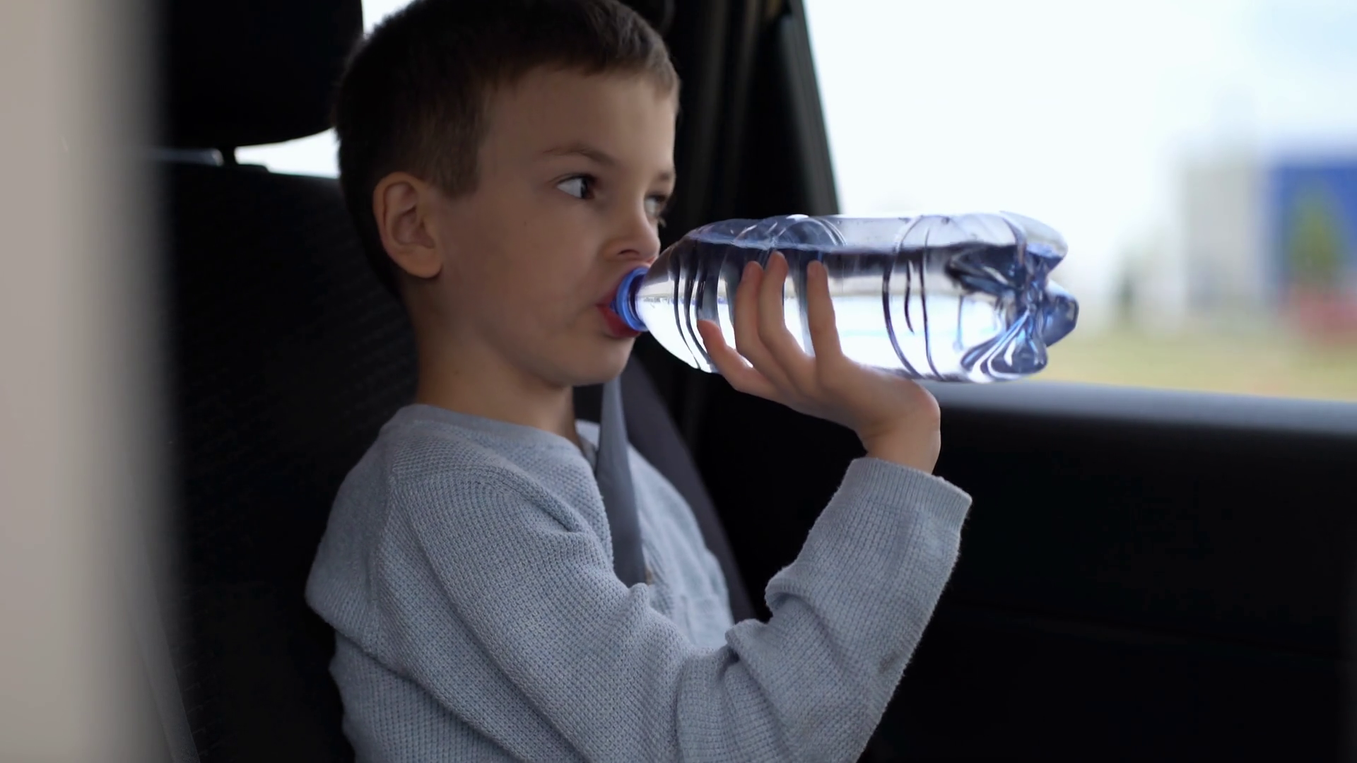 Boy drinking fresh water from a plastic bottle in the car. The child