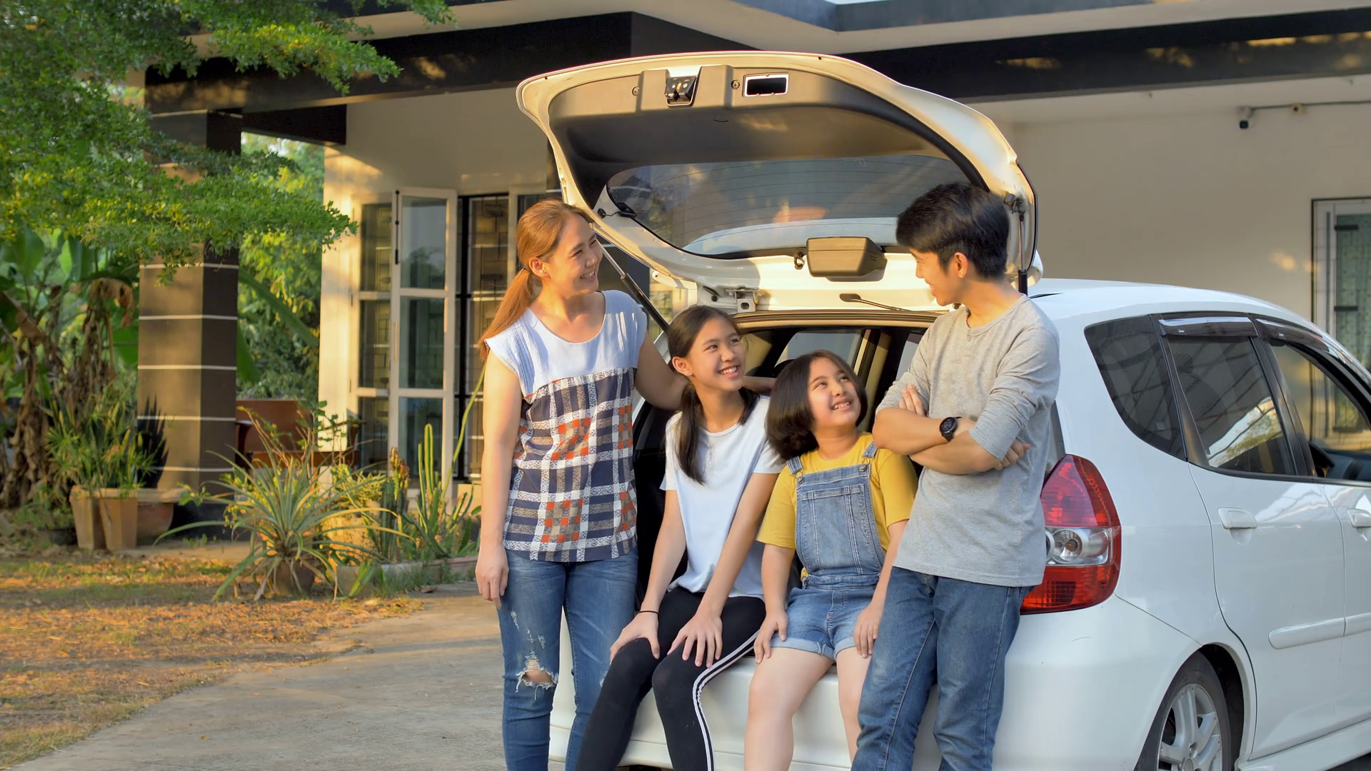 4K Happy family sitting on the car front of home Stock