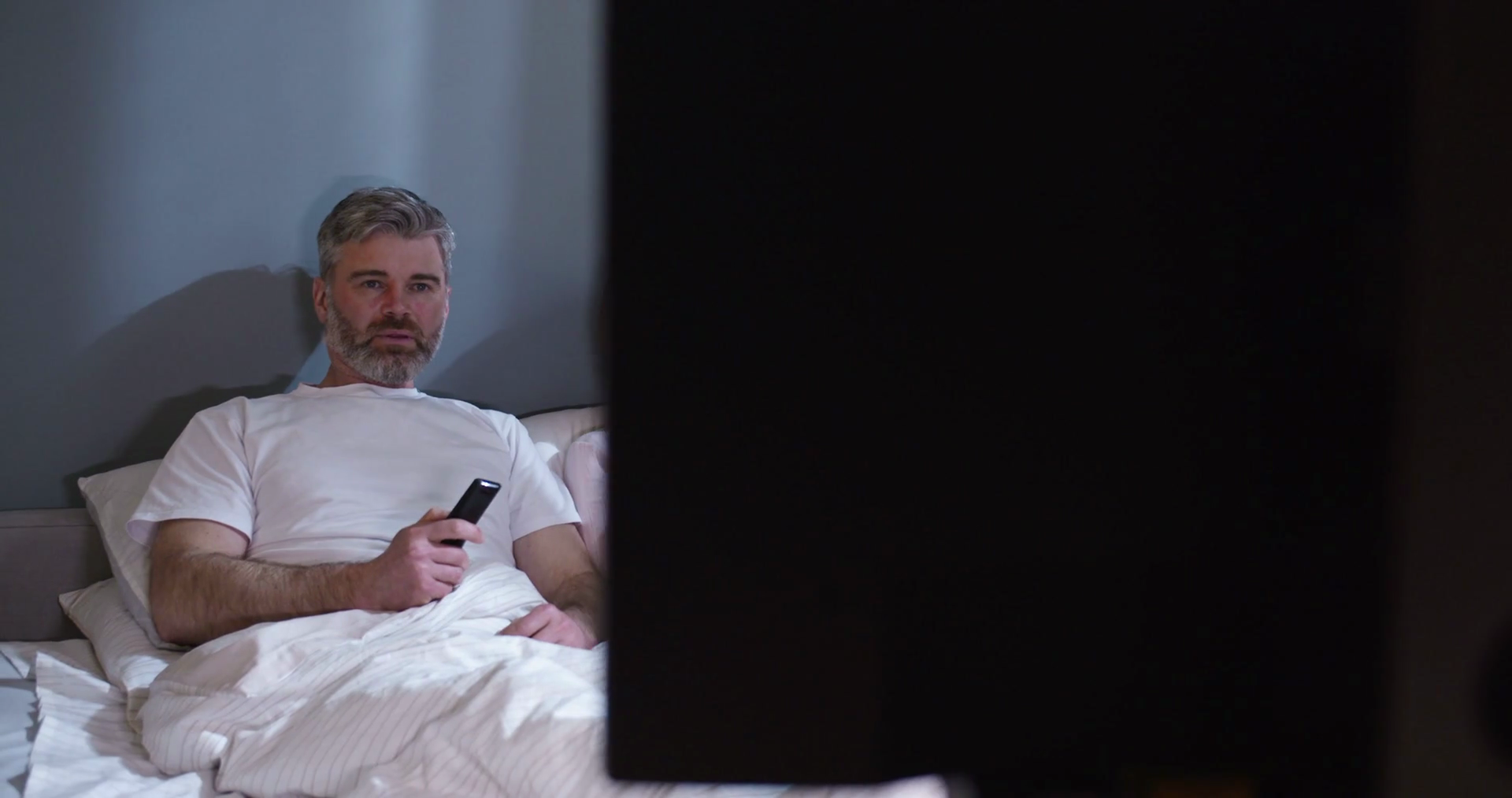 Husband and wife laying in bed watching TV smiling. Loving spouses