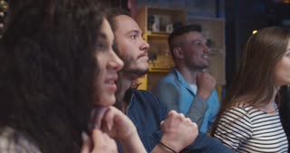 Caucasian guys and girls sitting at pub with beer in evening and watching sport match on TV. Friends celebrating football victory in bar. Male and female cheerful and happy fans.