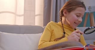 Cute child laughing and exploring with magnifying glass. Kid reading and smiling. Girl expressing at home. Small reader.