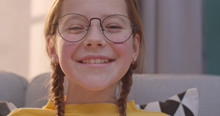 Close up of cheerful teen girl reading a book and smiling at the camera in a cozy living room