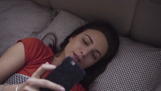 Woman using mobile device in bed, reacting with a smile