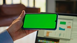 Unknown guy watching mockup smartphone sitting at desk closeup. Unrecognizable person looking webinar on green screen mobile phone at home