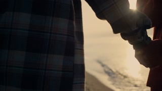 Unrecognizable couple walking on ocean beach at sunset. Closeup woman and man holding hands together. boyfriend and girlfriend dating at sea shore. Girl holding smartphone. Romantic concept