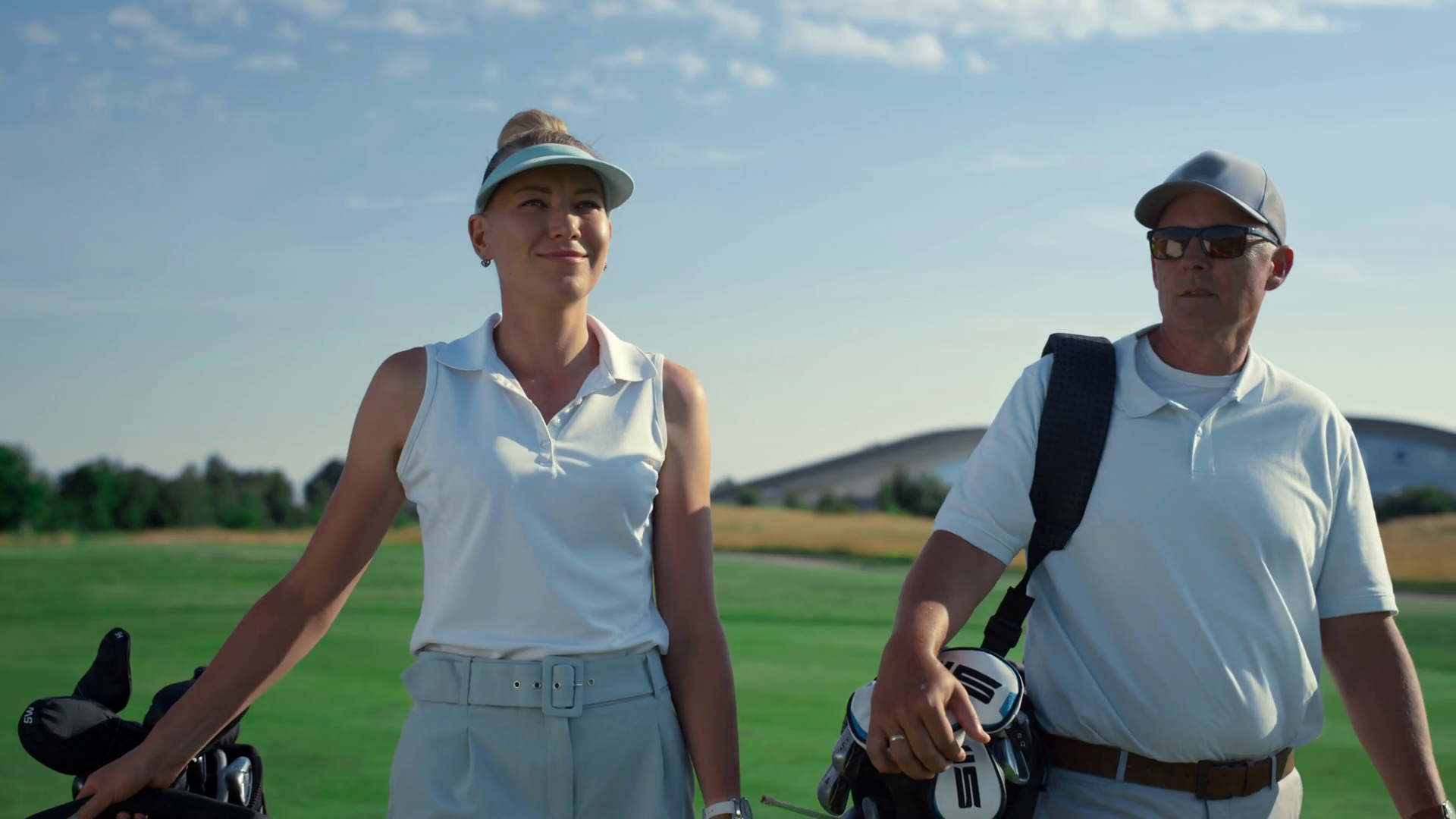 Golf players couple walk together on lush course. Rich people talking