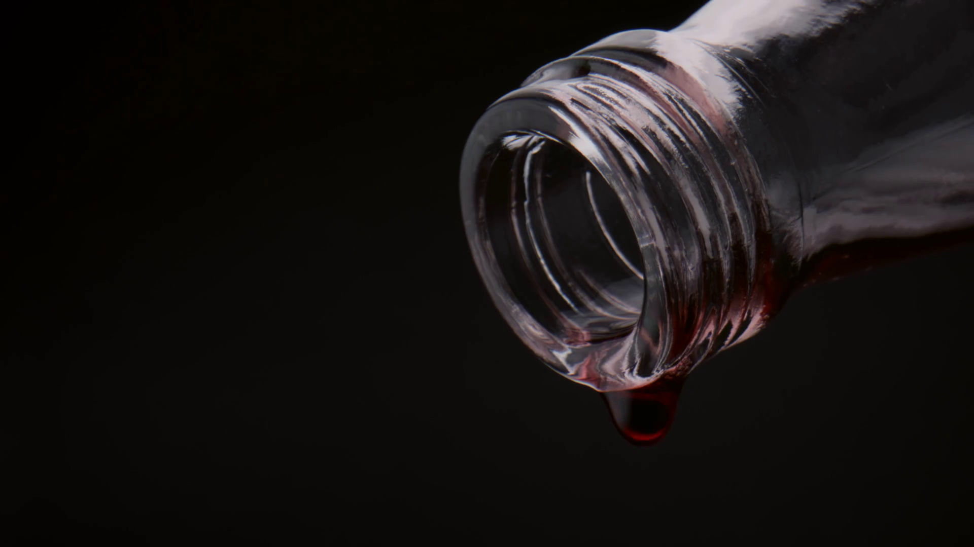 Closeup red wine drops falling down from glass bottle neck in super