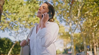 Closeup view of confident middle aged businesswoman talking on smartphone while walking in city park. 