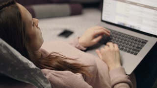 Business woman browsing internet on computer screen at home. Woman lying on sofa with laptop computer at night. Professional freelancer working remote with data analytics