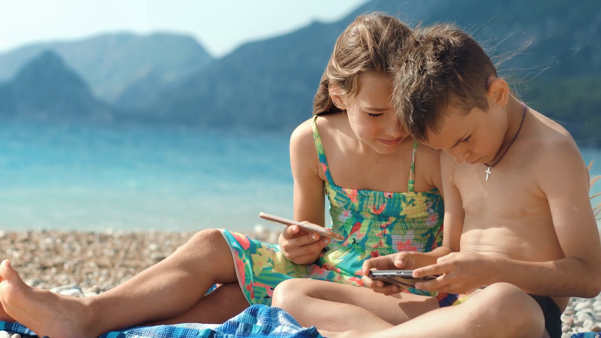 Happy kids play games on mobile phone at sea beach. Sister and brother  enjoying summer vacation at ocean with mountains on background. Children  playing smartphone game together Stock Video Footage 00:20 SBV-331416137 -