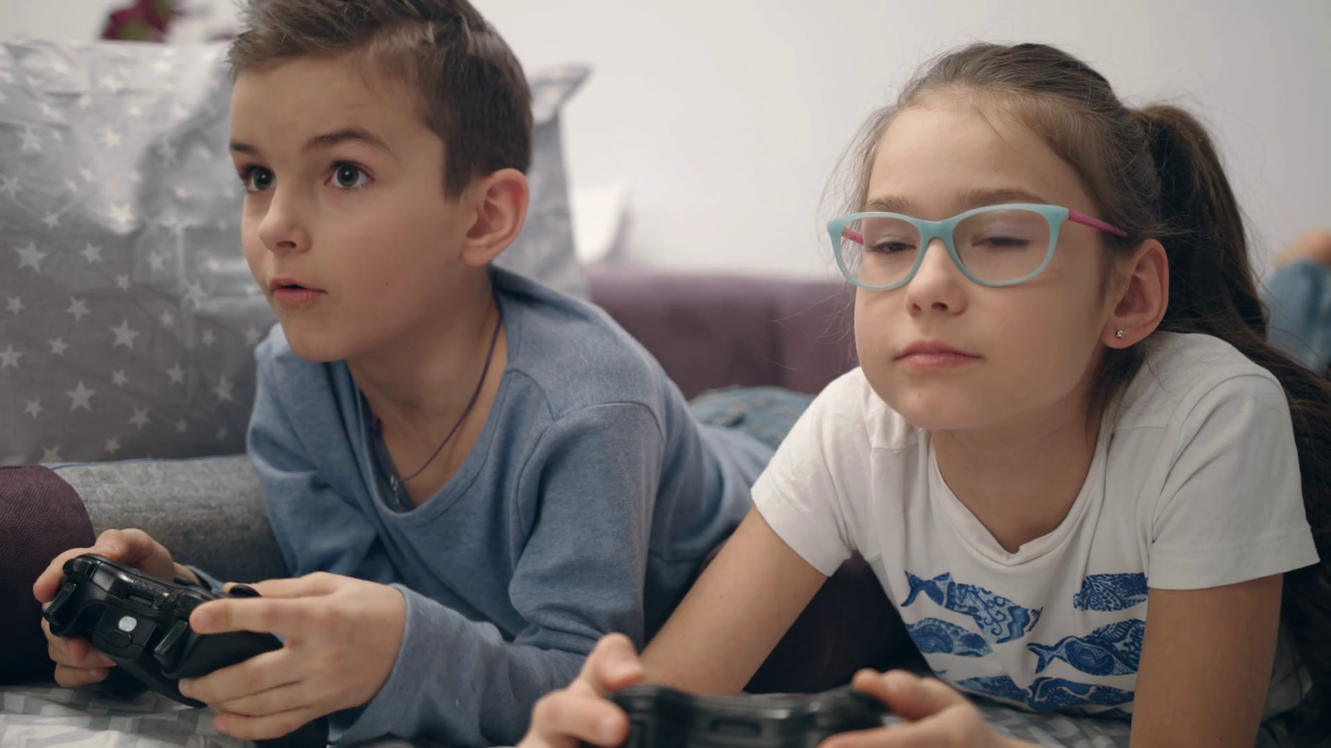 Siblings enjoy video game at home. Girl close eyes boy. Brother and sister  playing video game on sofa. Kids have fun together with joystick. Kids  using gamepad at home Stock Video Footage