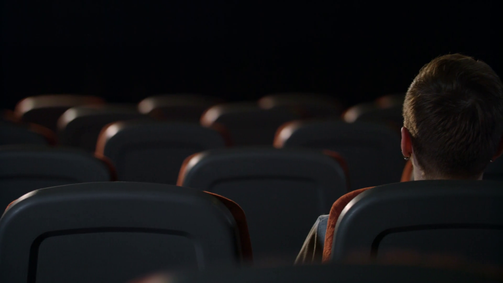 Stylish guy sitting in empty movie theater alone. Back view of man head in cinema. Lonely guy