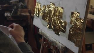 Senior artist on a wheelchair applies gold to the oil painting